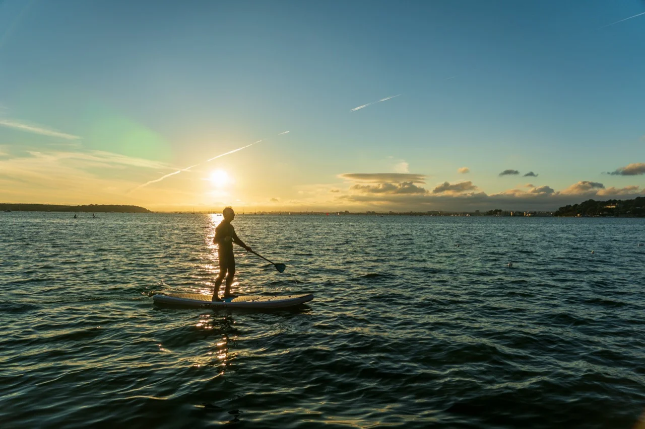 A paddleboarder on open water in golden evening light