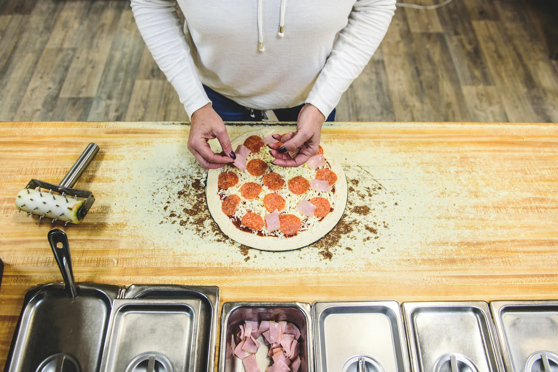 Hands adding toppings to a pizza on a floured worktop