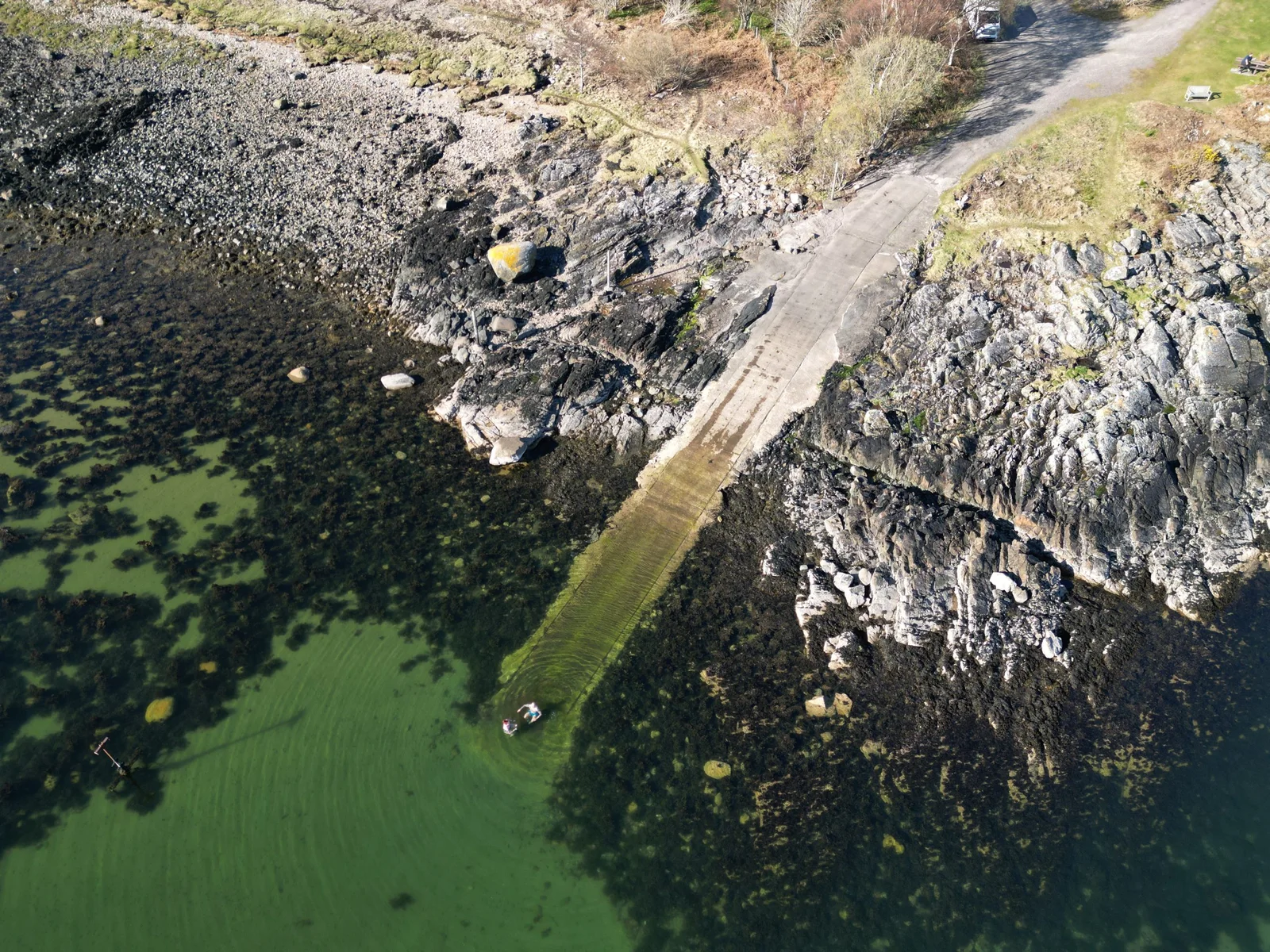 An aerial view of the slipway and rocky shoreline beside clear coastal water at Tralee Bay